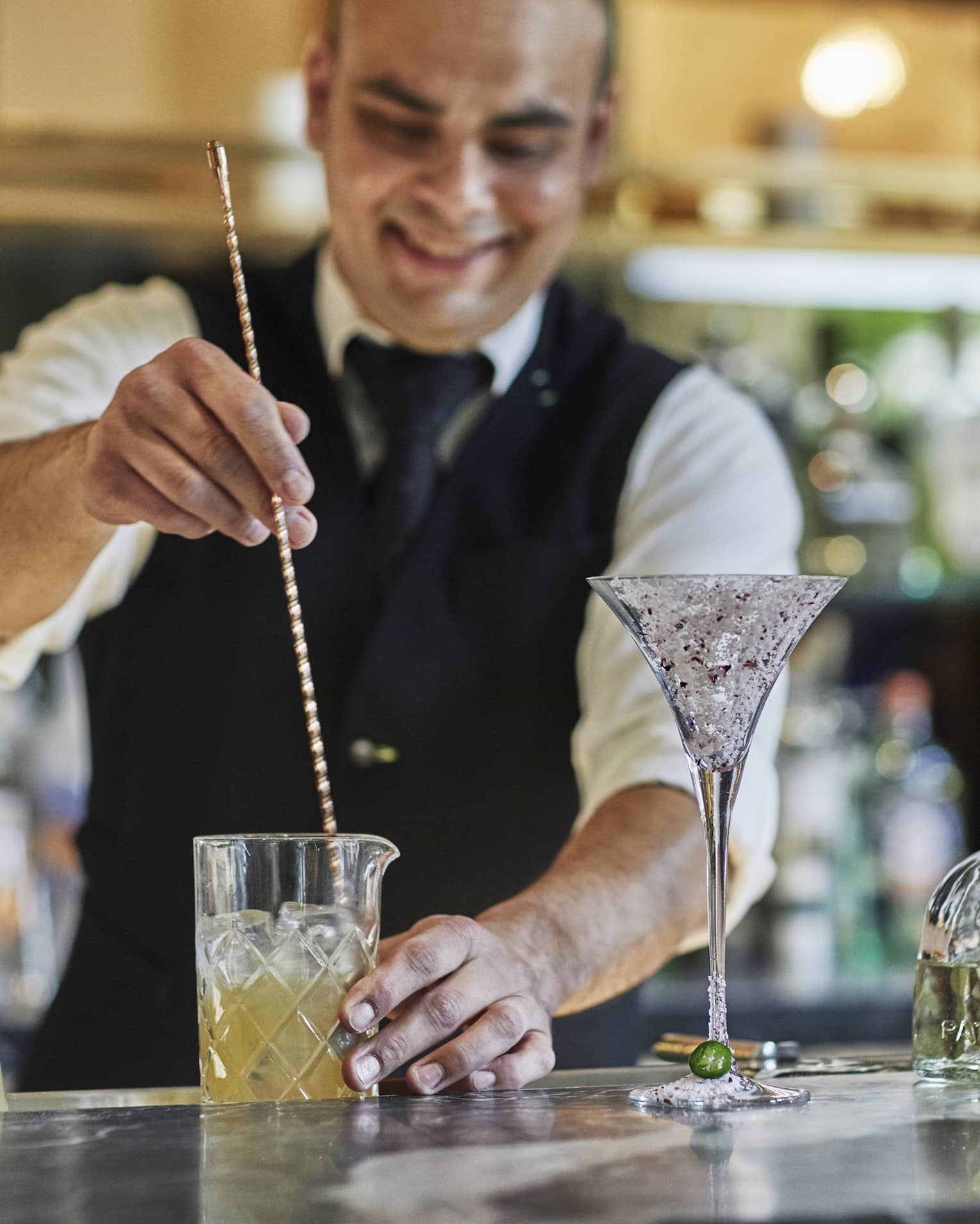 Bartender stirs cocktail with large swizzle stick on bar 