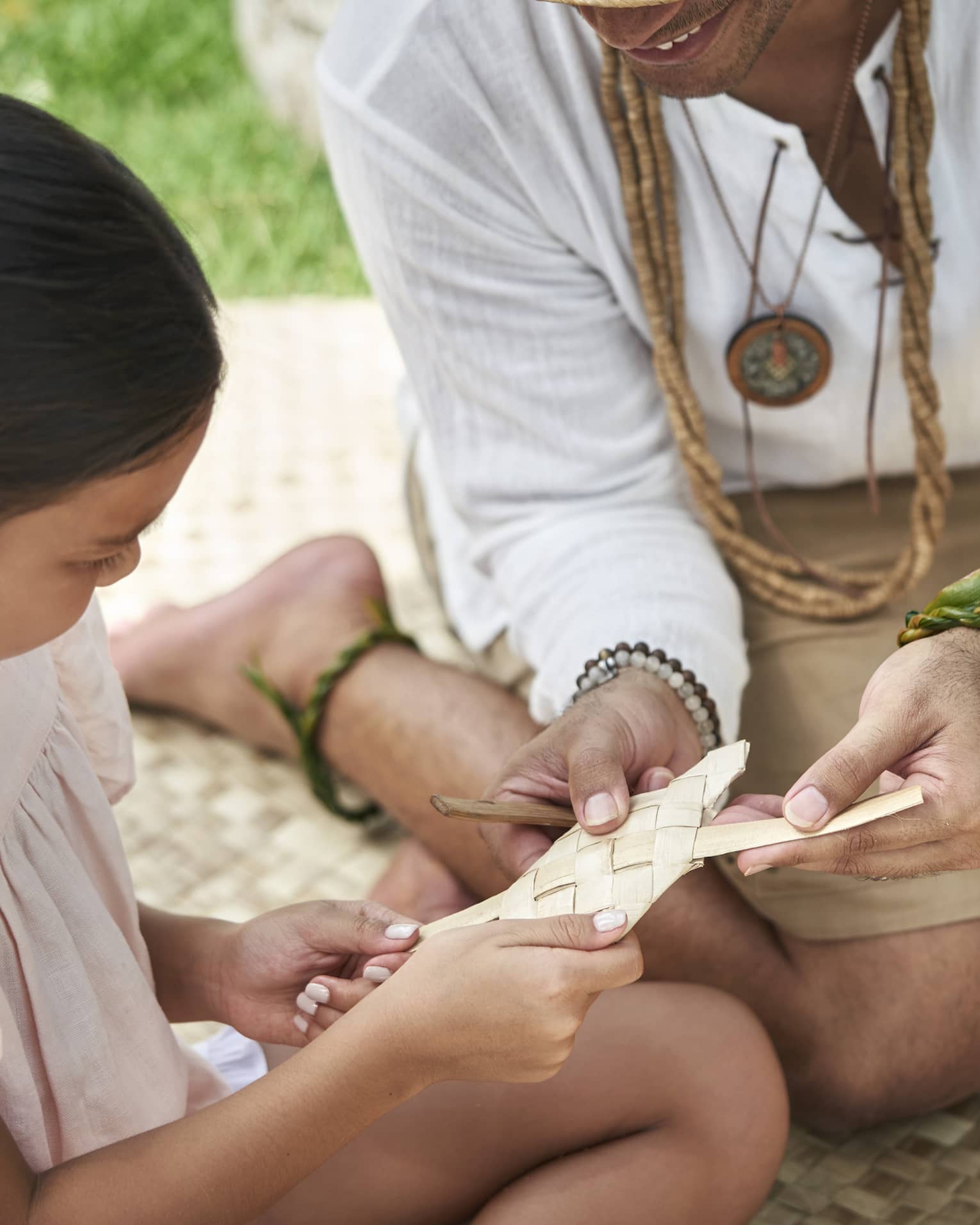 An adult shows a young girl how to weave a basket