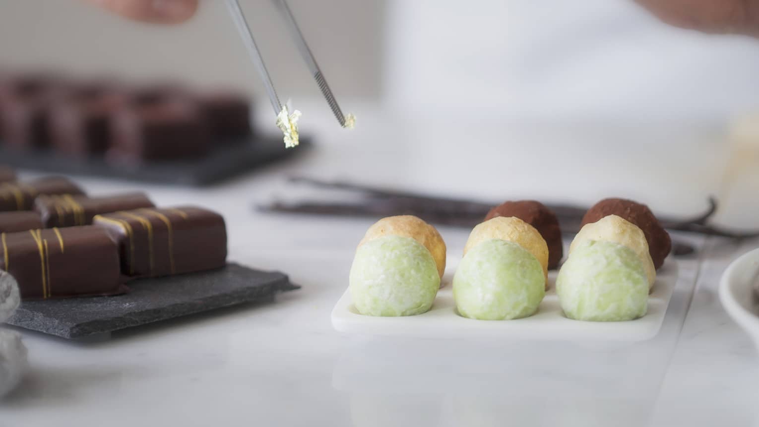 A close up of a male chef's hands using tongs to place various chocolates on parchment paper