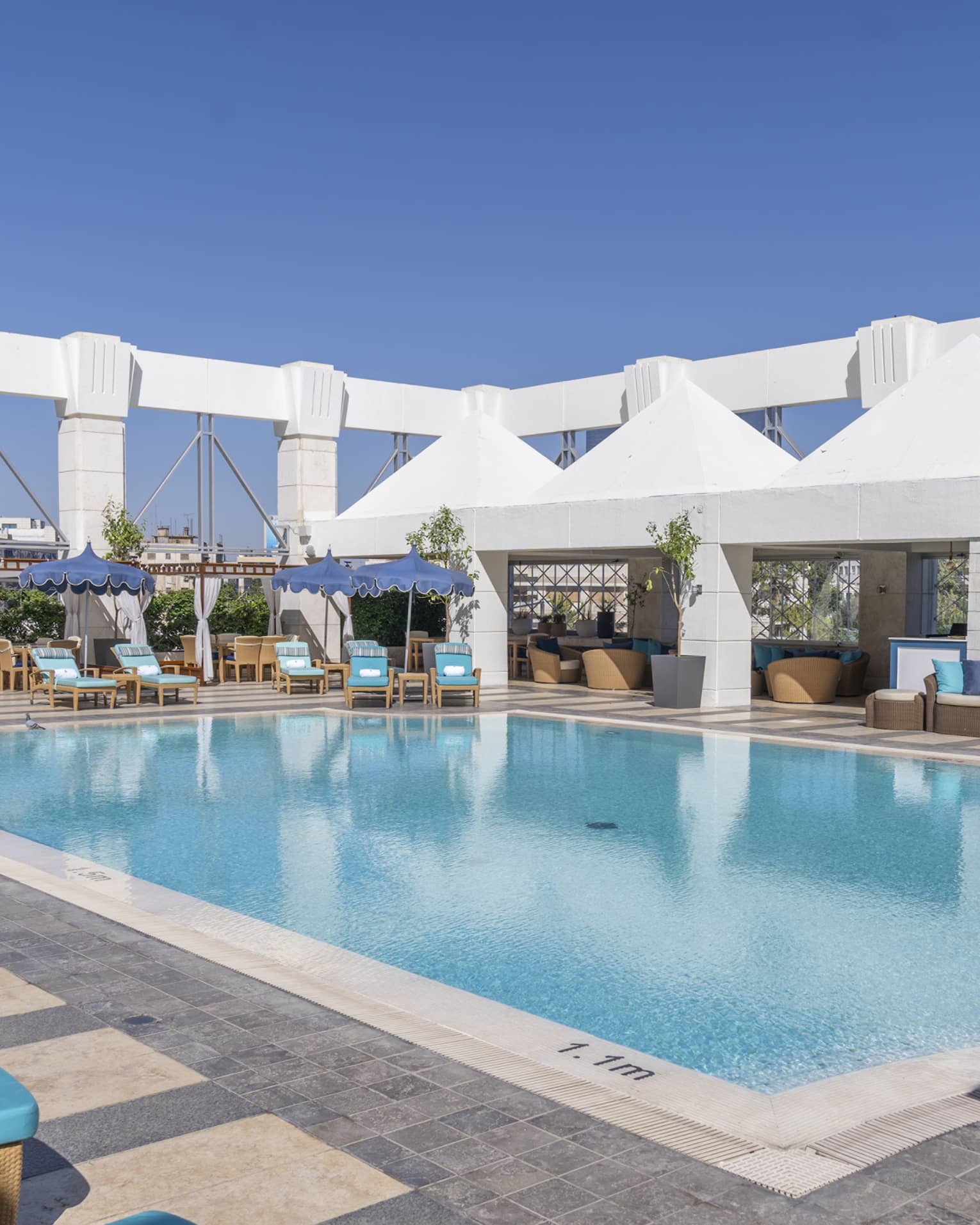Outdoor pool surrounded by blue lounge chairs and four white tents