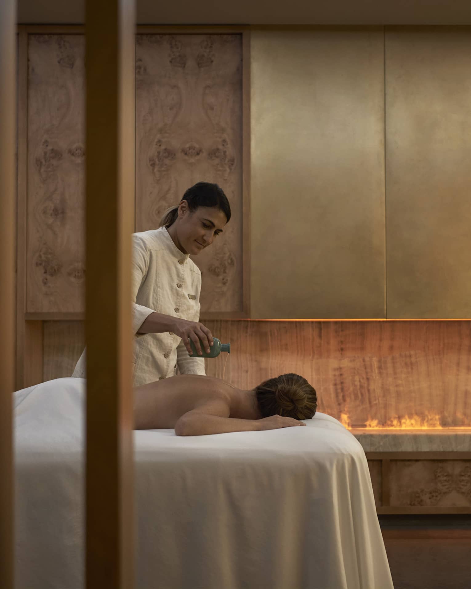 Spa therapist pours oil on back of person facedown on spa table