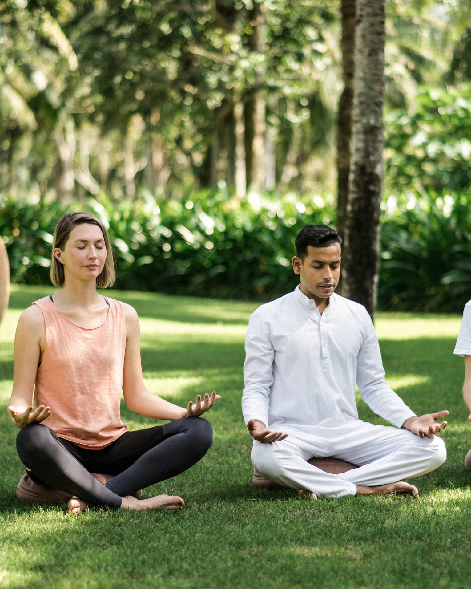 Two men and a woman practise meditation yoga outdoors on lawn