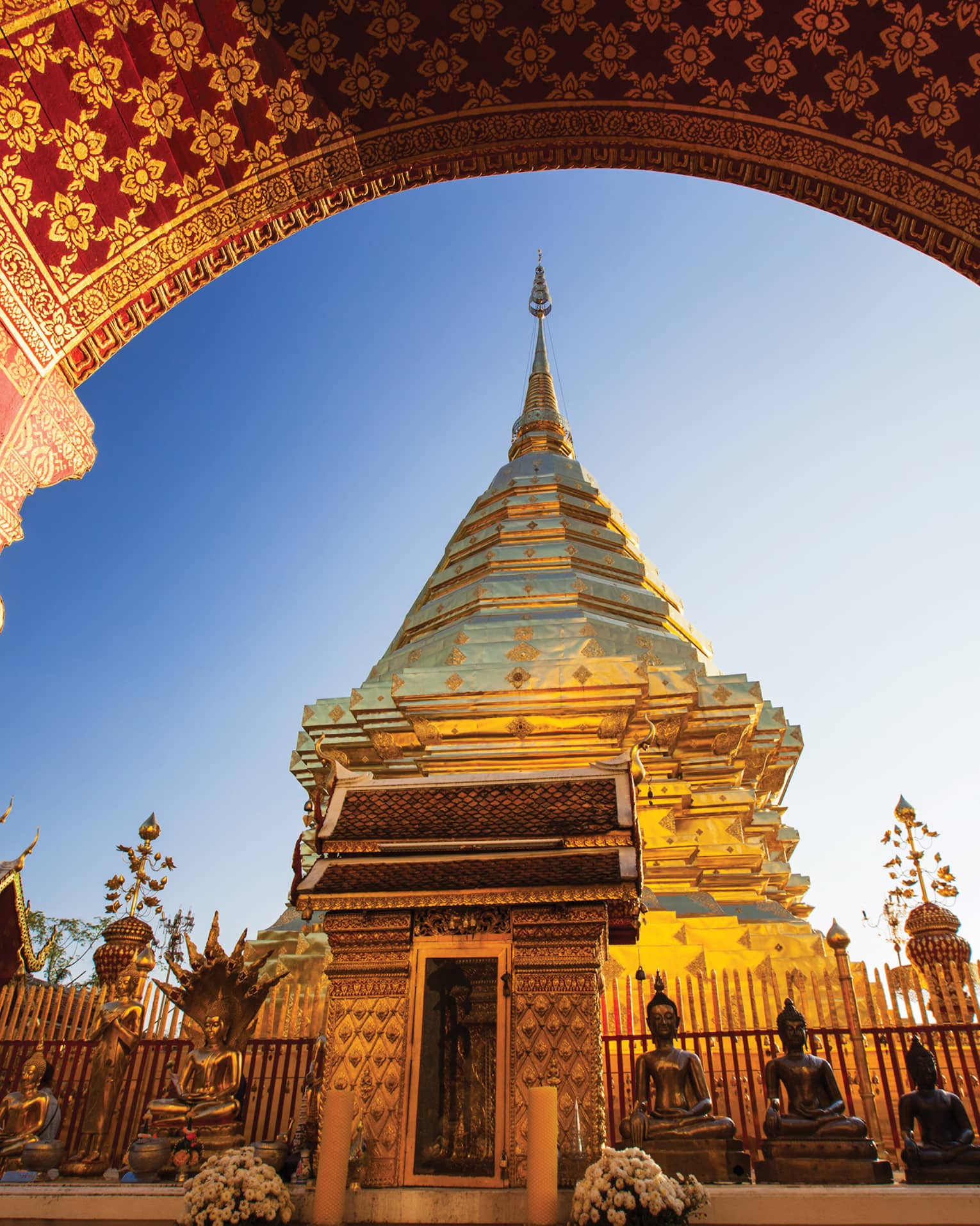 View from under painted arch looking up at golden Wat Phra That Doi Suthep historic Buddhist temple, statues 