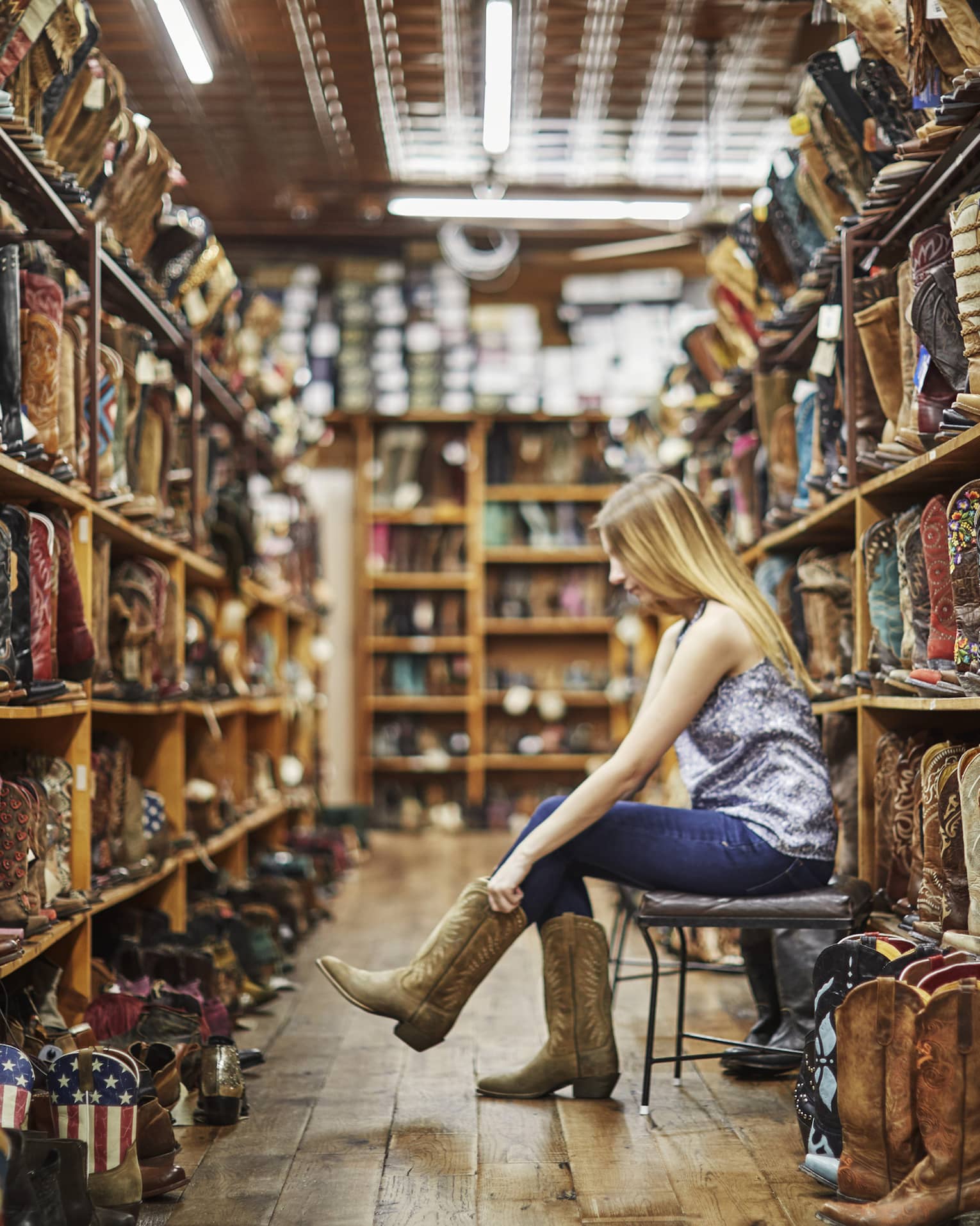 A woman trying on cowboy boots in a store full of them.