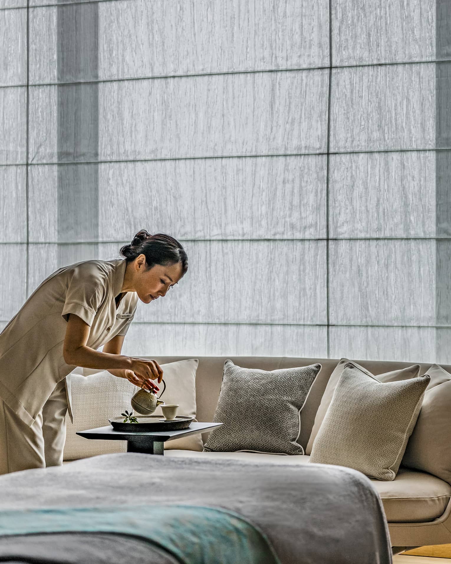 Spa team member pours hot tea into a cup, a cream couch and treatment table in the background 