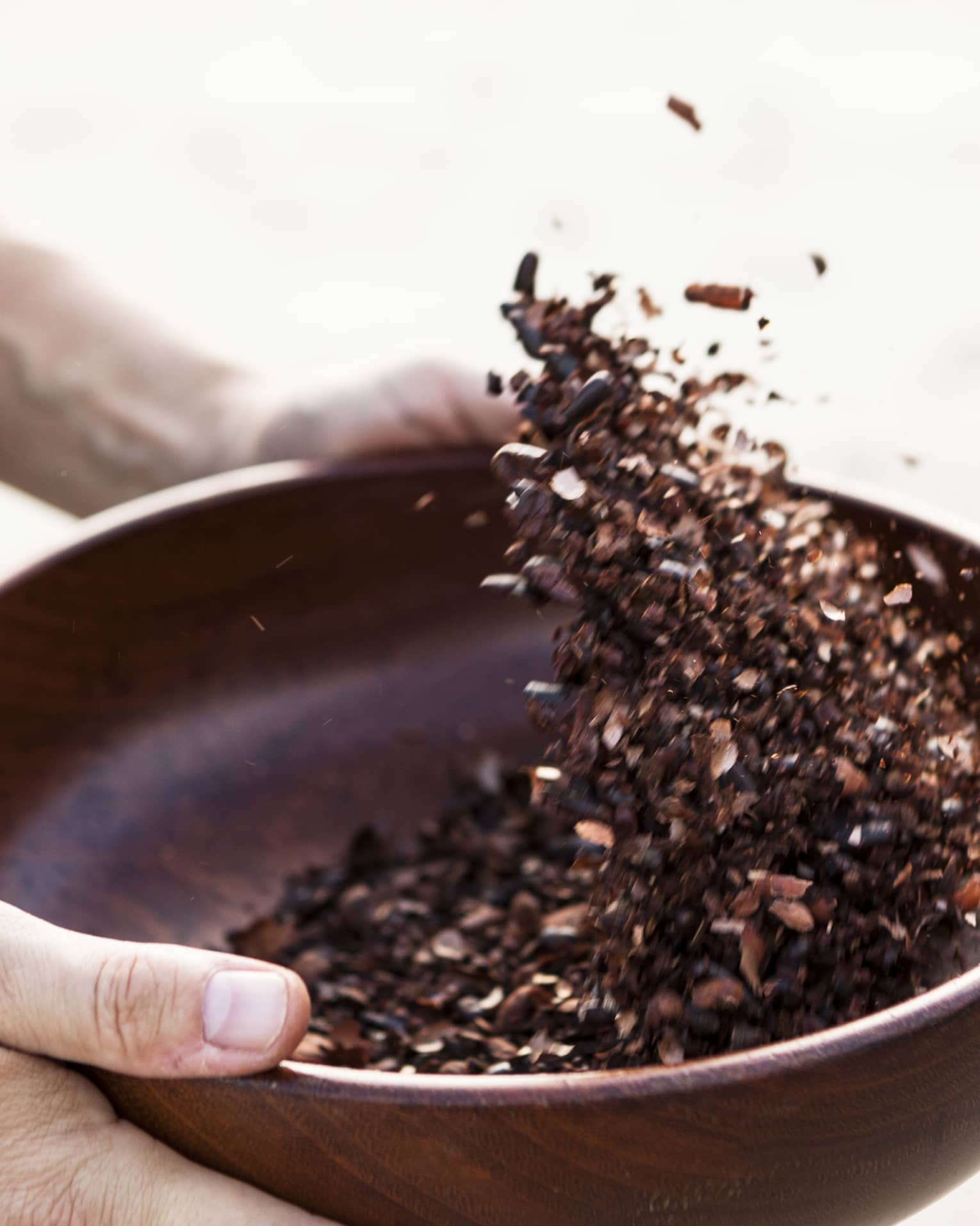 Close-up of hands holding dark wood bowl, shaking crushed cocoa