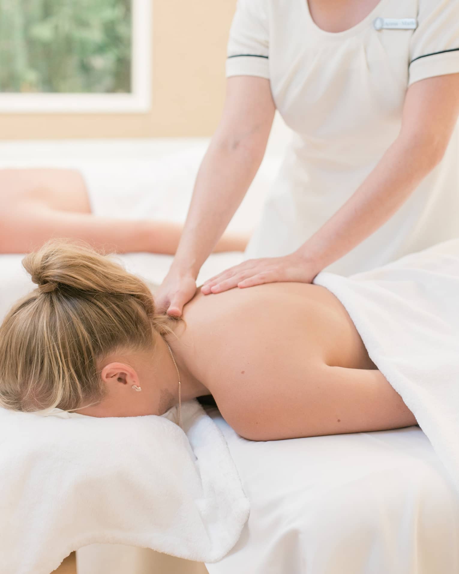 Couple laying on massage tables, spa staff massages woman's shoulders 