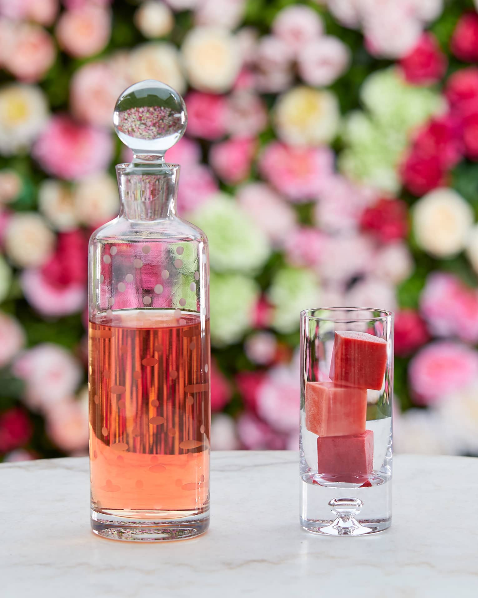A cocktail and glass bottle in front of a wall of roses.