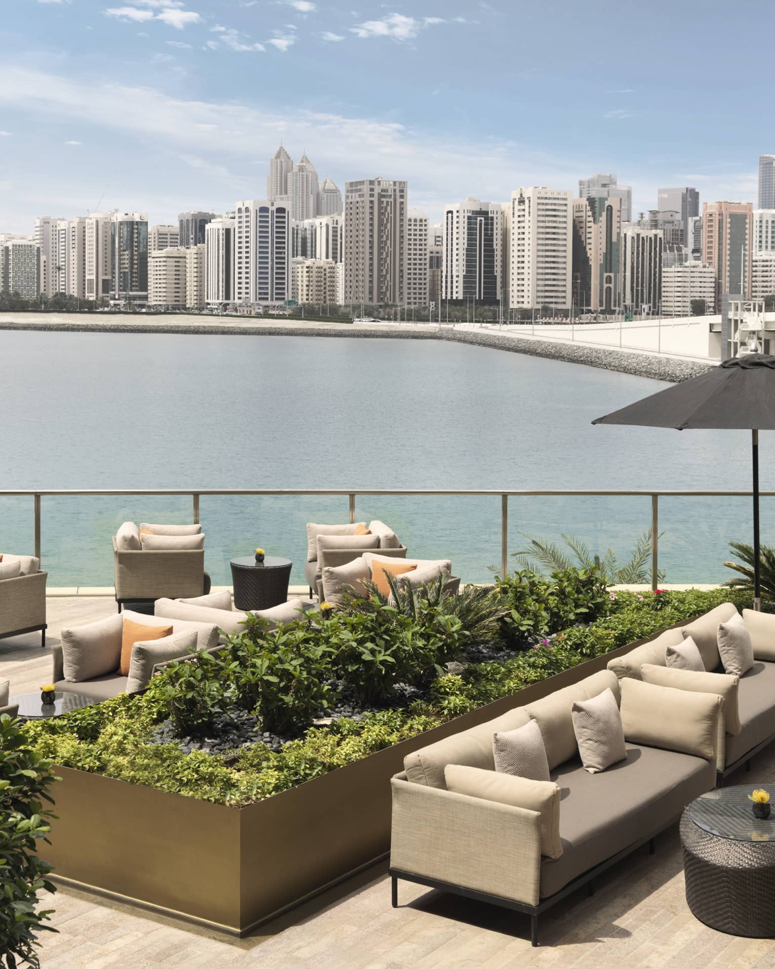 Outdoor sofas, umbrellas and planters on patio overlooking water, city