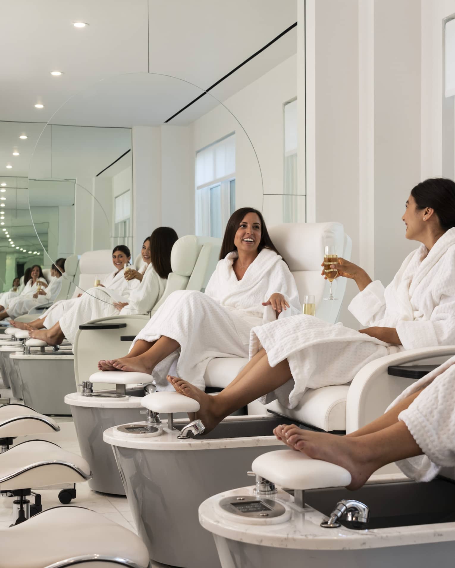 Three women wearing bath robes sit in pedicure spa chairs