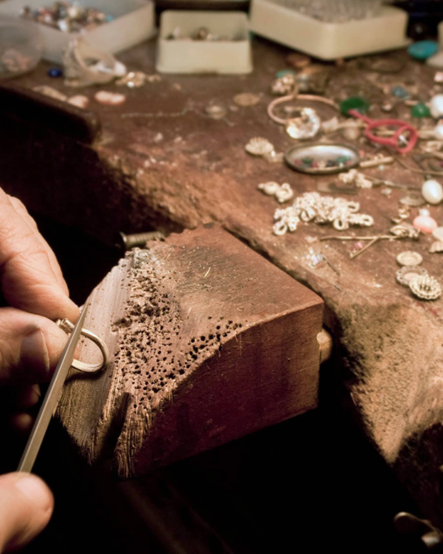 Jeweller's hands using a tool to craft jewellery on a wooden block