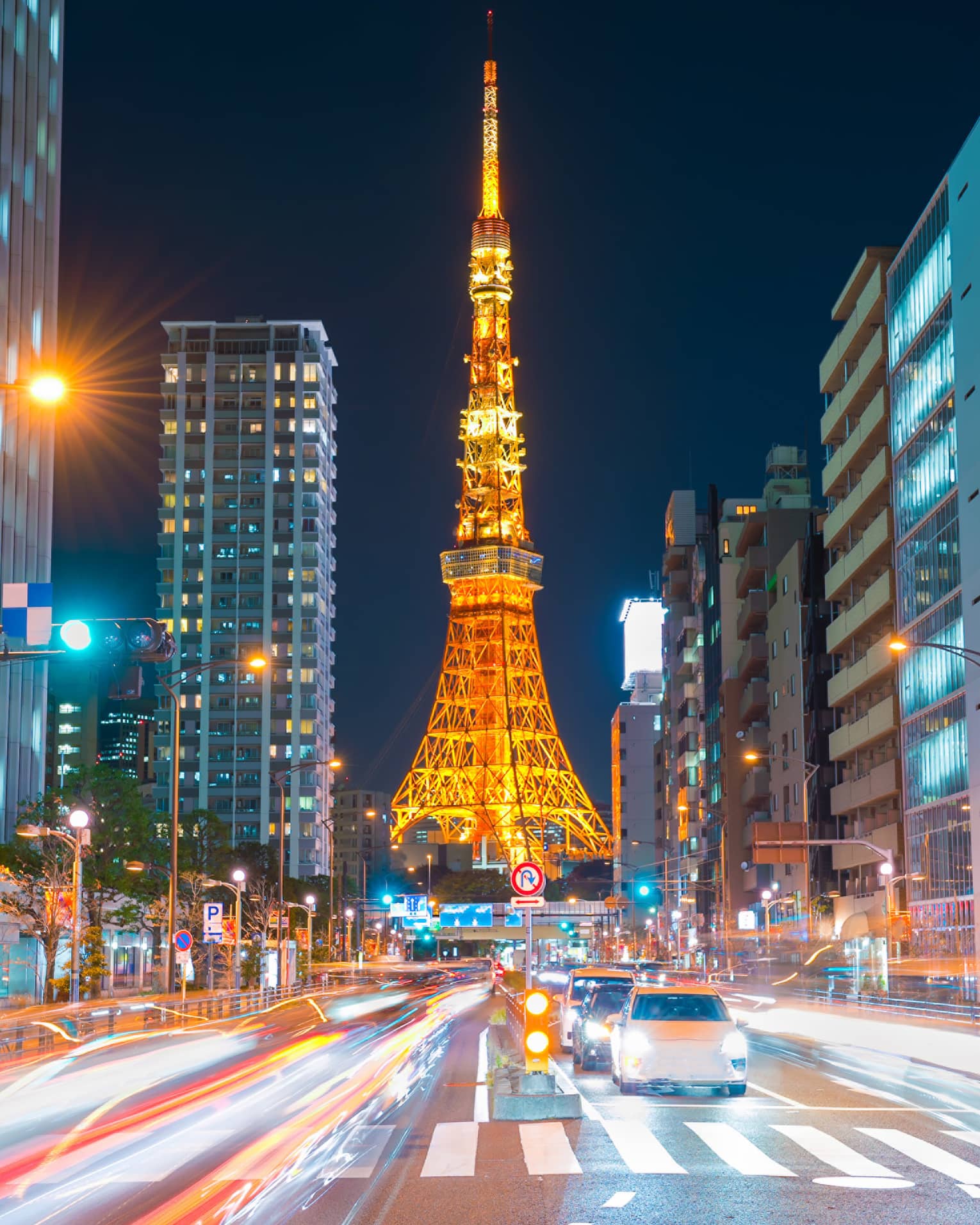 Long view down a brightly-lit street, the Tokyo Tower at the bottom, glowing in orangey hues against an inky-black sky.