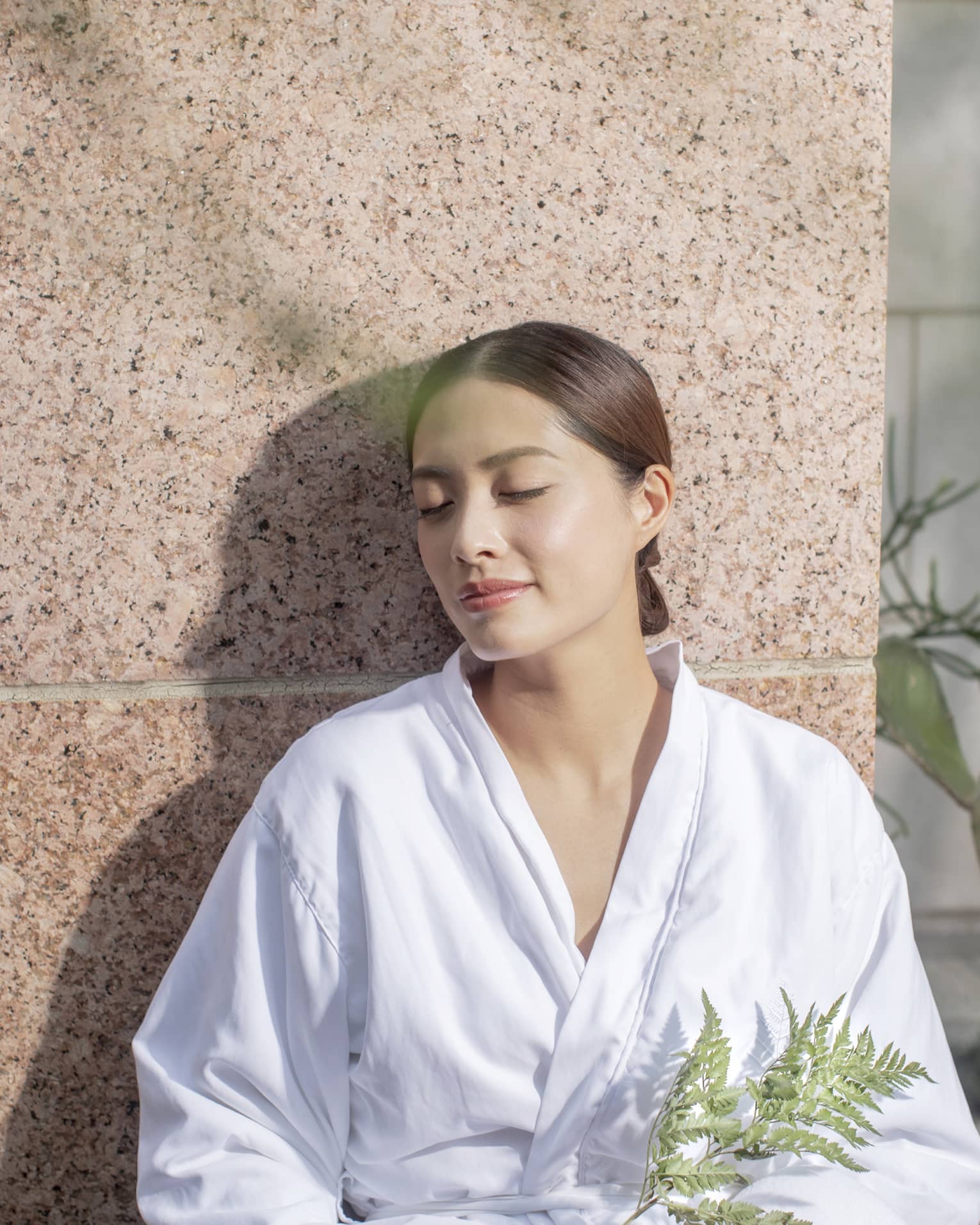 A woman resting outside near plants in a spa robe.