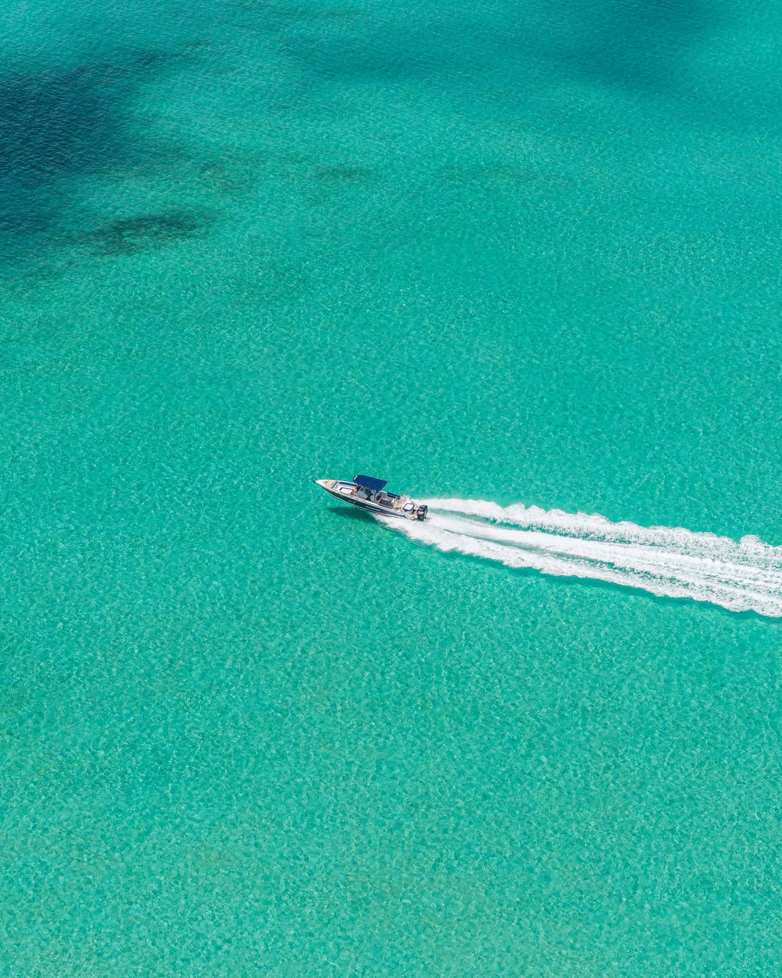 Aerial view of a speedboat moving through a vast expanse of turquoise water, followed by a substantial wake trail.