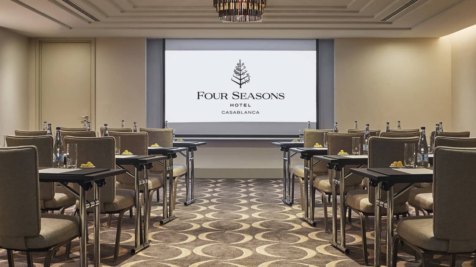 Rows of chairs, tables facing large screen with Four Seasons logo