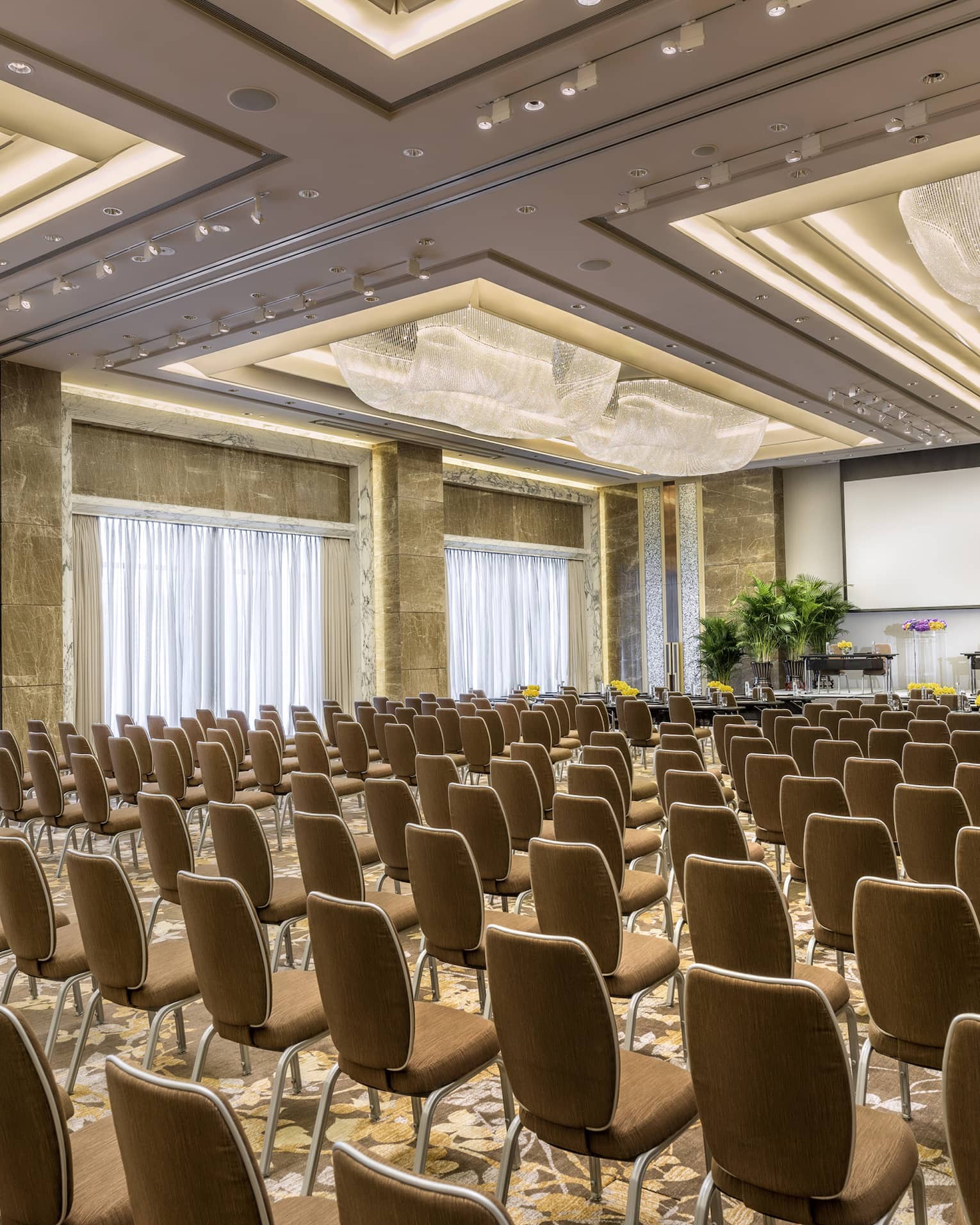Rows of meeting chairs facing screen, potted trees in large Four Seasons Ballroom 