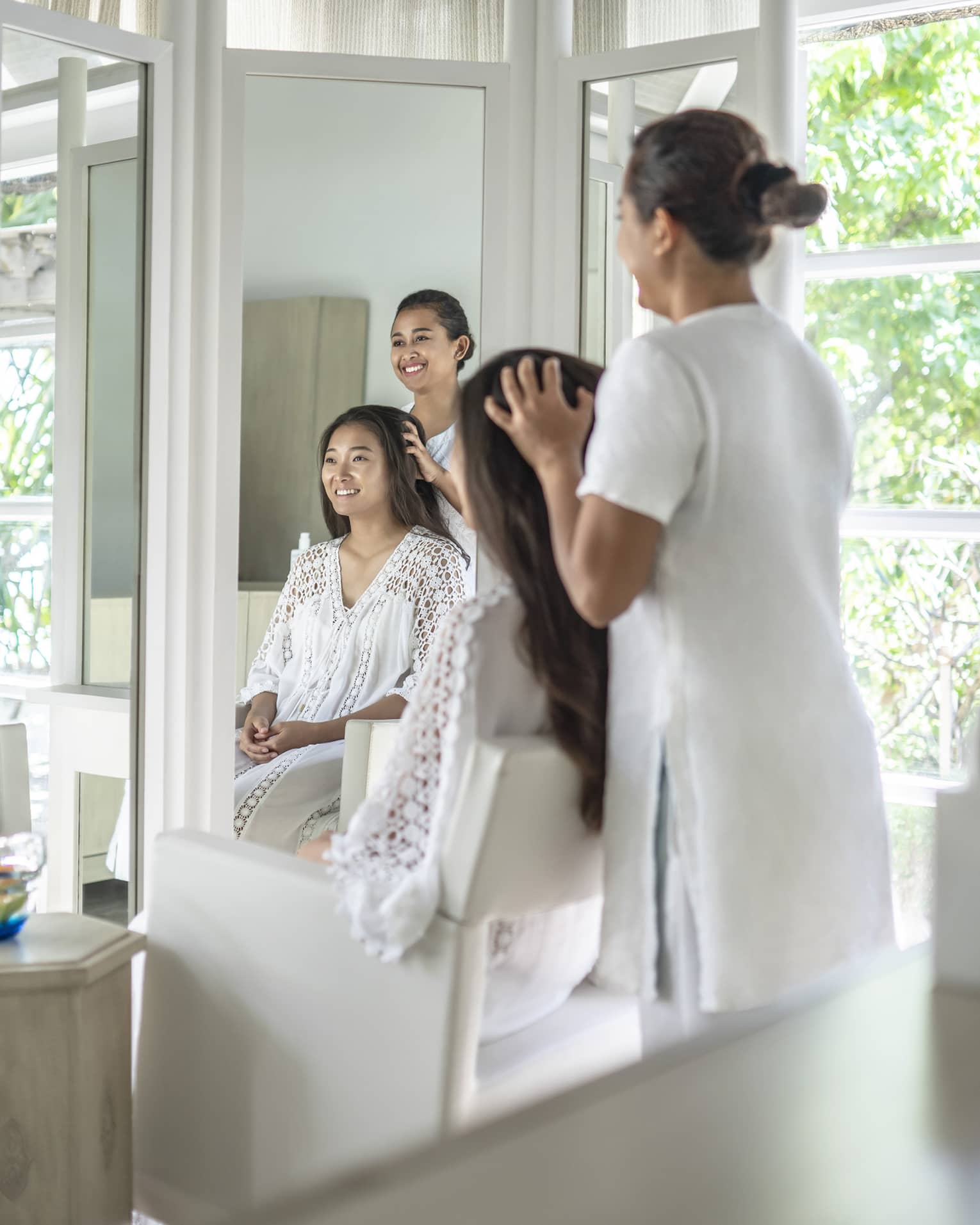 A four seasons guest gets her hair done while sitting in a white salon chair facing floor to ceiling windows revealing greenery just outside the salon