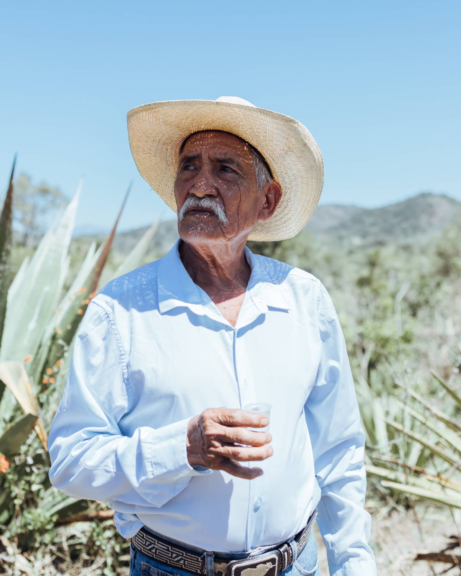 Person wearing a hat and a blue button down shirt standing outside.