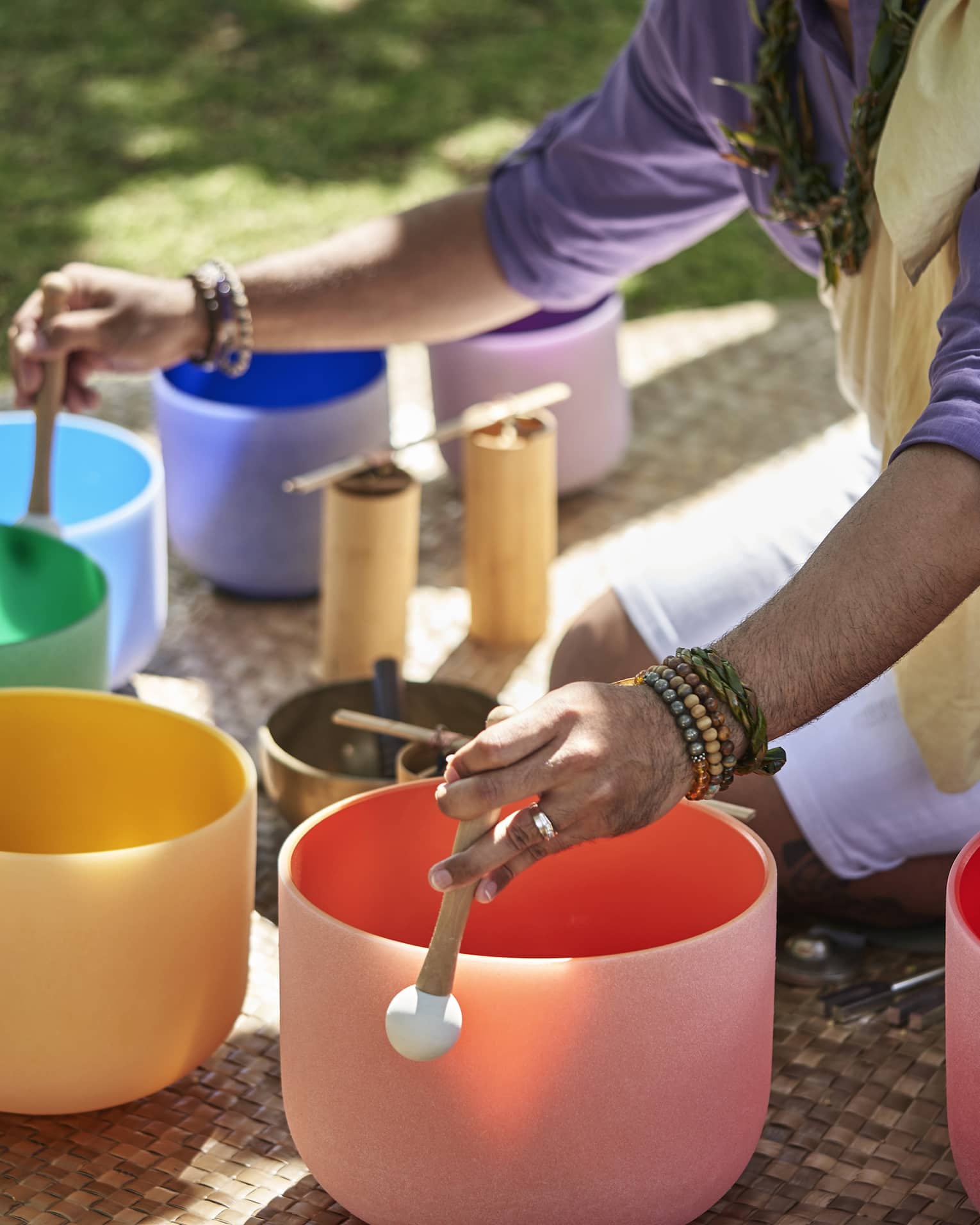 Close up of a man's hands using mallets to play a row of colourful crystal sound bowls