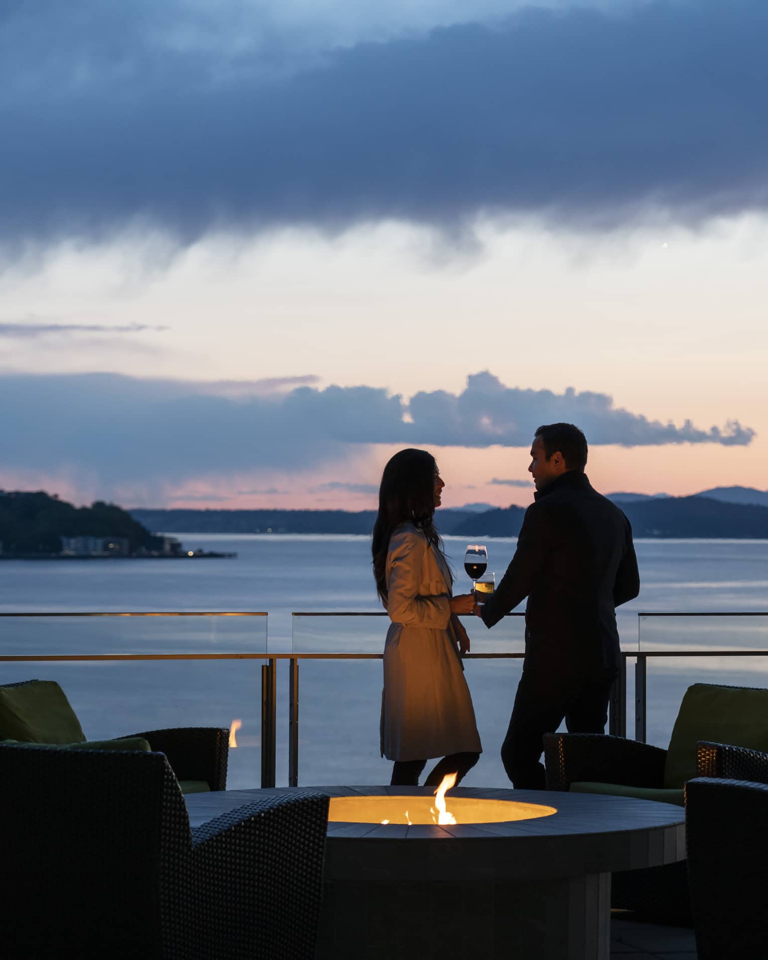 A couple holds hands and shares wine on the balcony as the sun sets