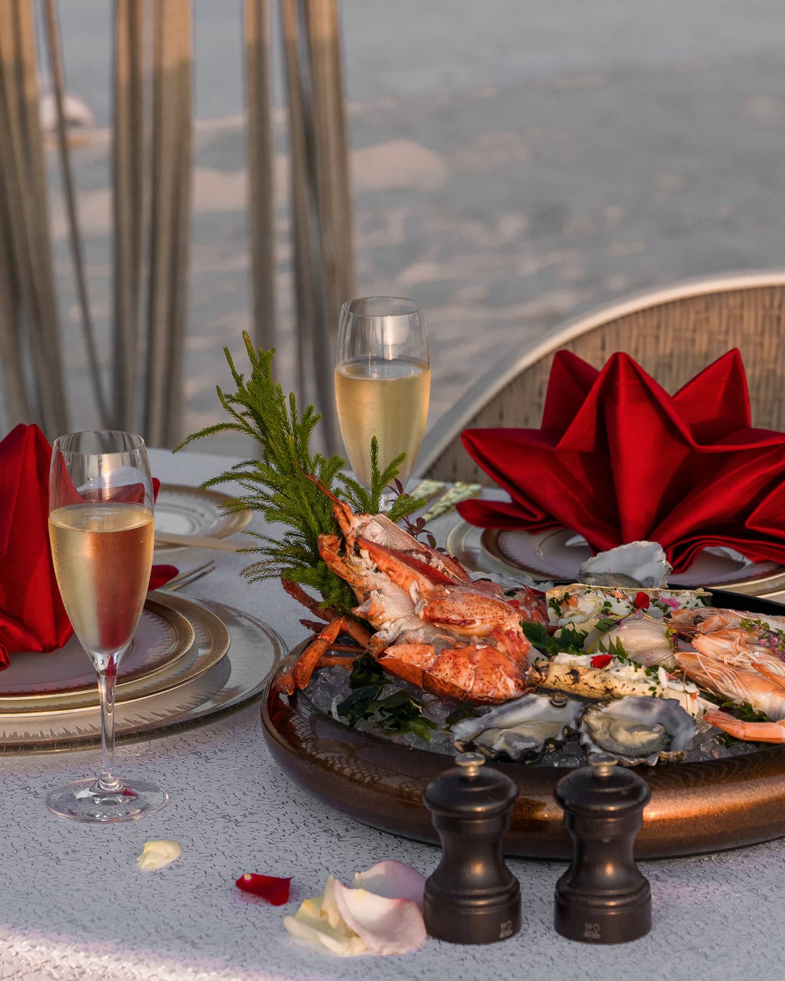 A table set on the beach with crab, champagne and red napkins.