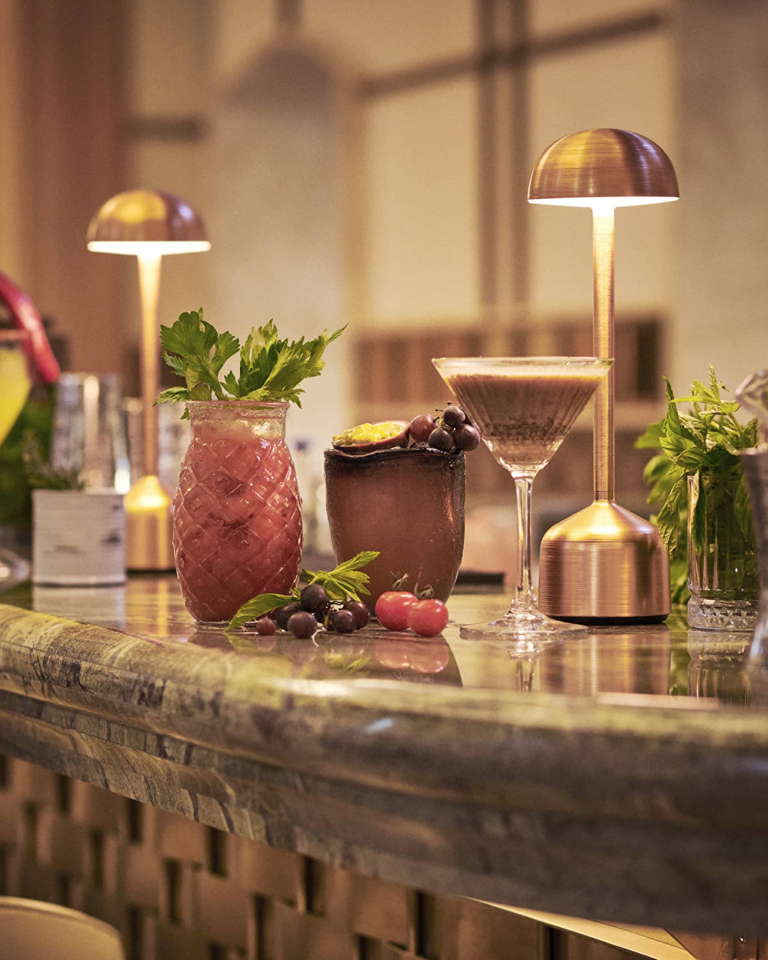 Cocktails in various glassware lined up on bar under copper desk lights