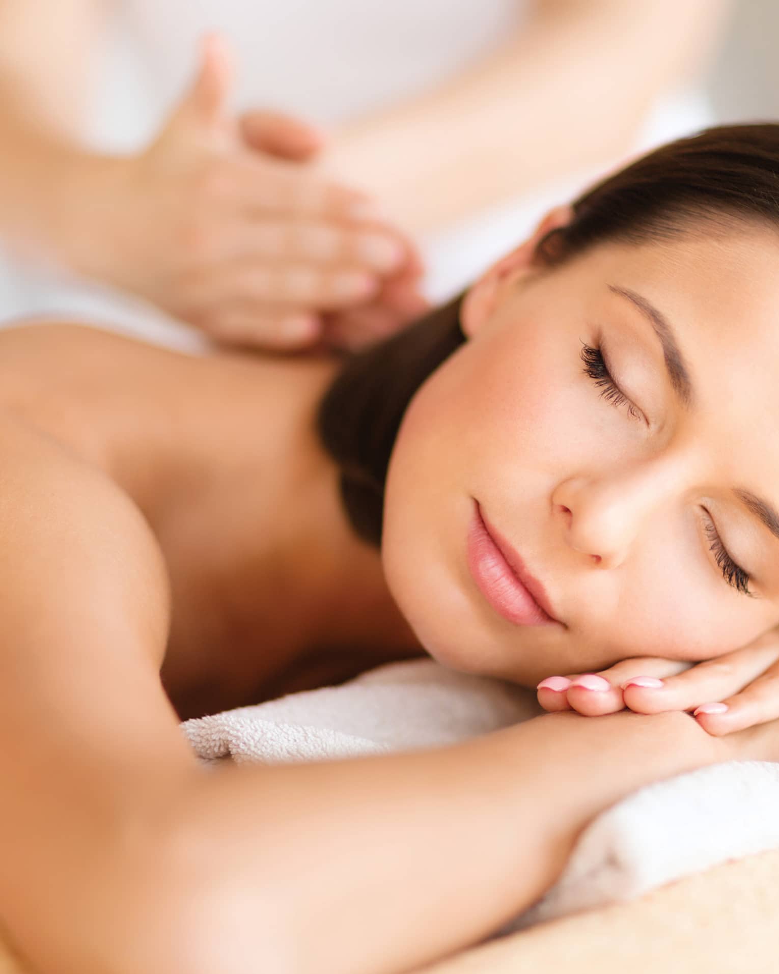 Woman lies on massage table, closes eyes. rests head on arms as spa staff massages back