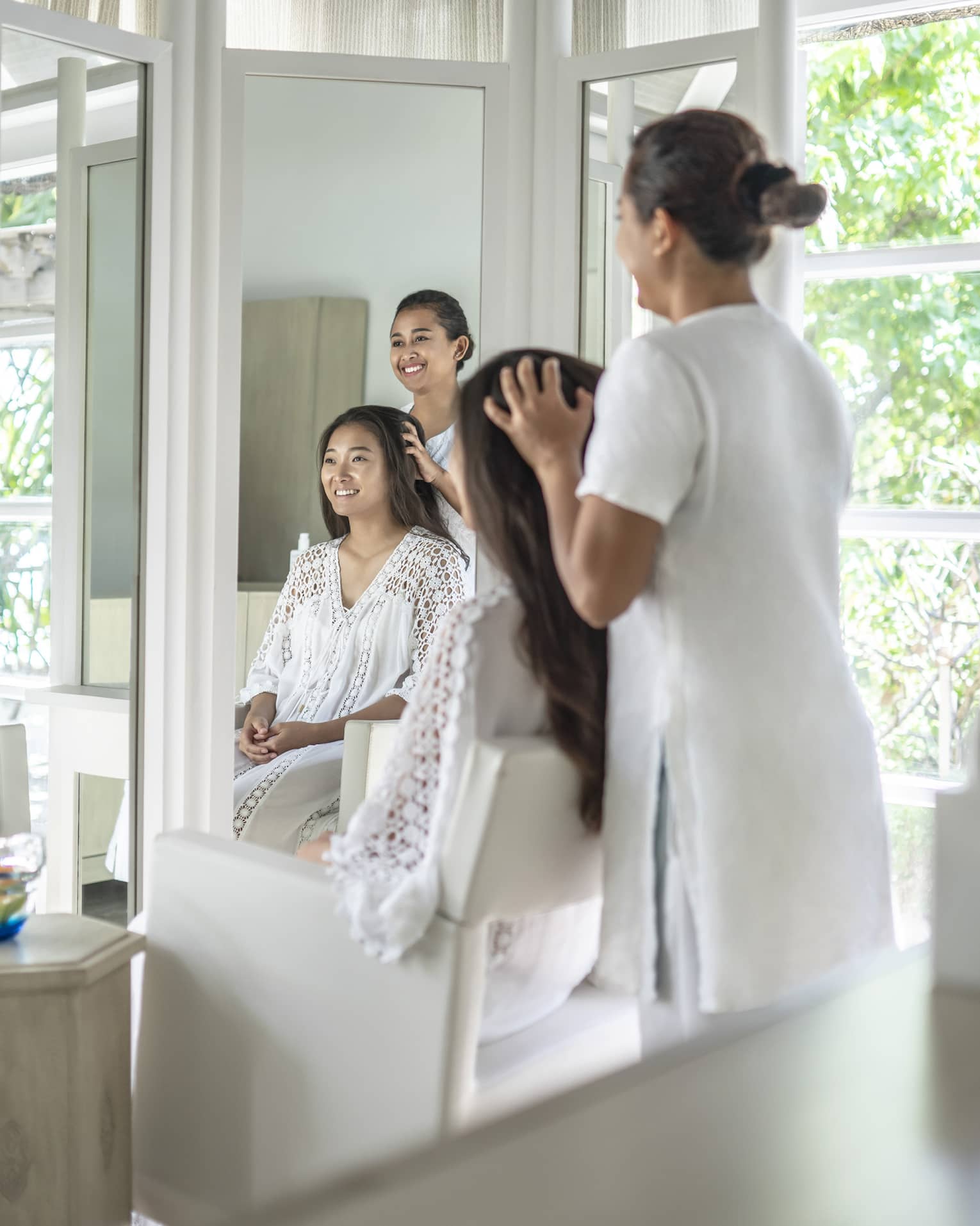 A four seasons guest gets her hair done while sitting in a white salon chair facing floor to ceiling windows revealing greenery just outside the salon