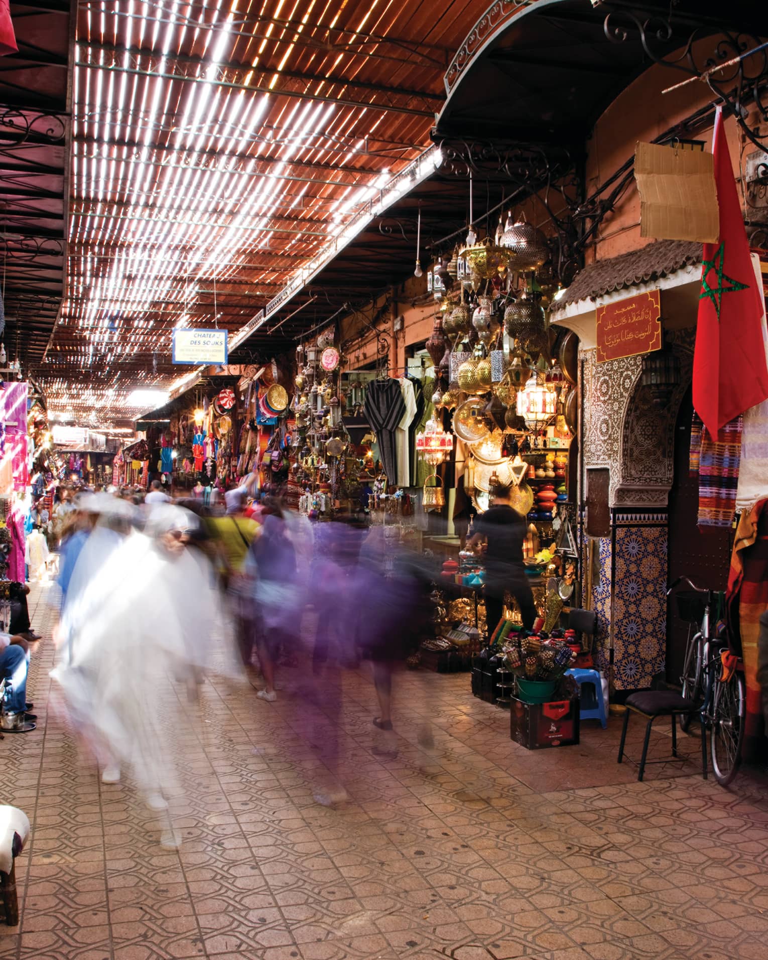 People walk through Moroccan market with stalls filled with colourful textiles, treasures