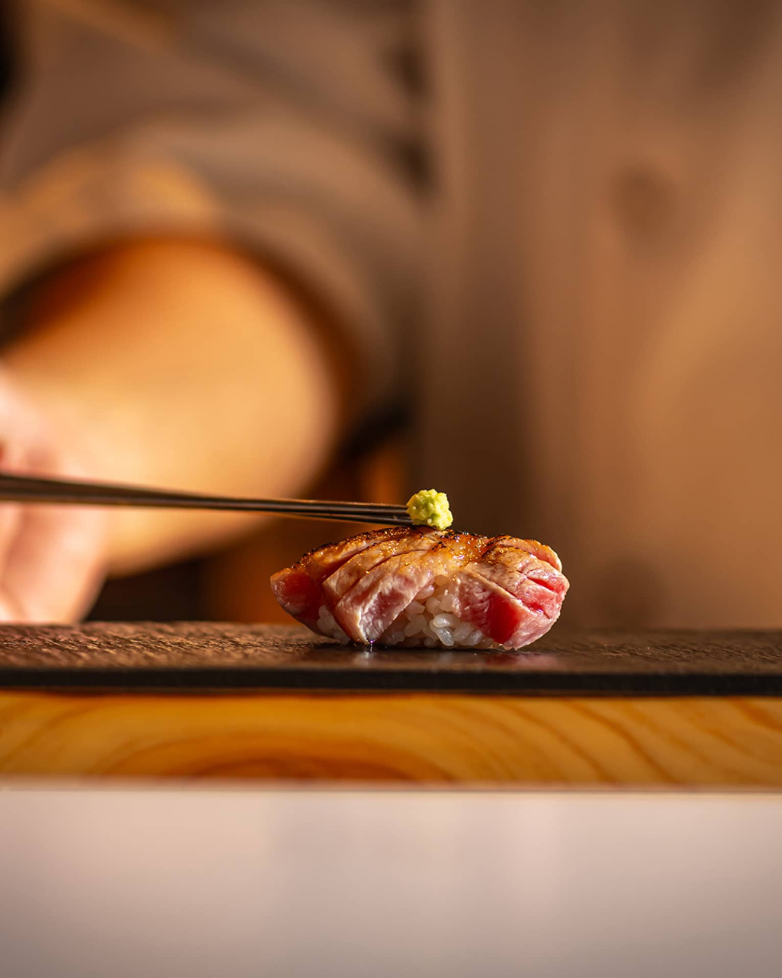 A person placing wasabi on a piece of sushi.