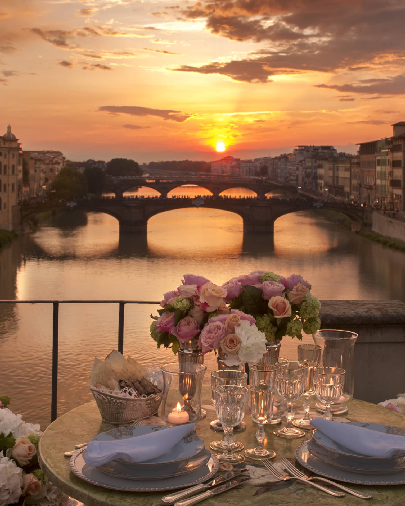 Pink roses in vases on formal dining table on bridge overlooking canal, sunset