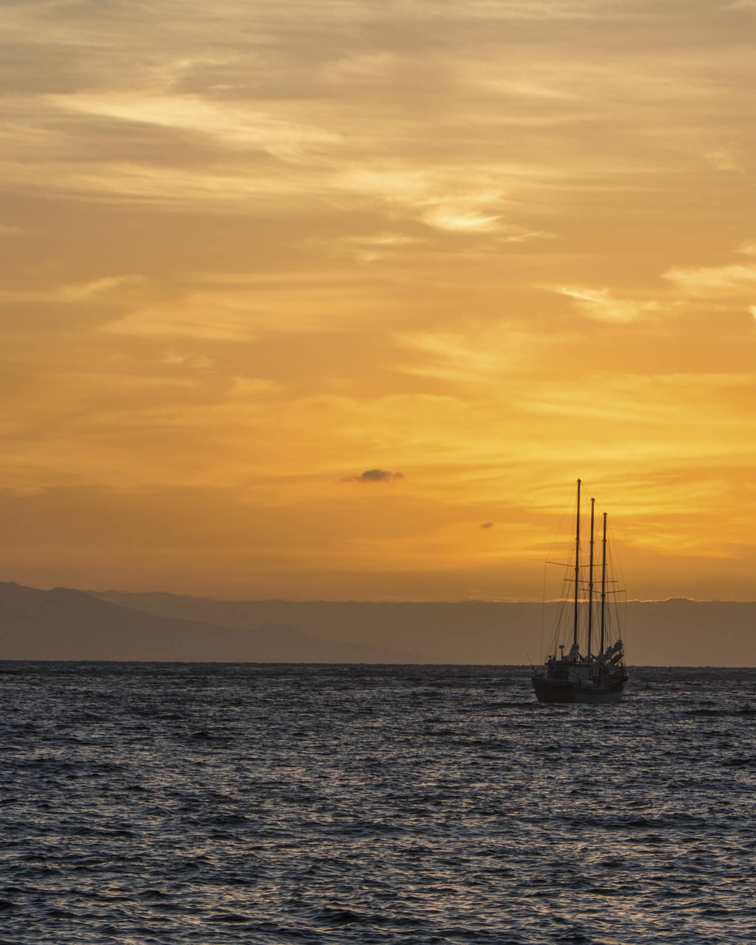 Sailboat silhouette on ocean against orange sunset