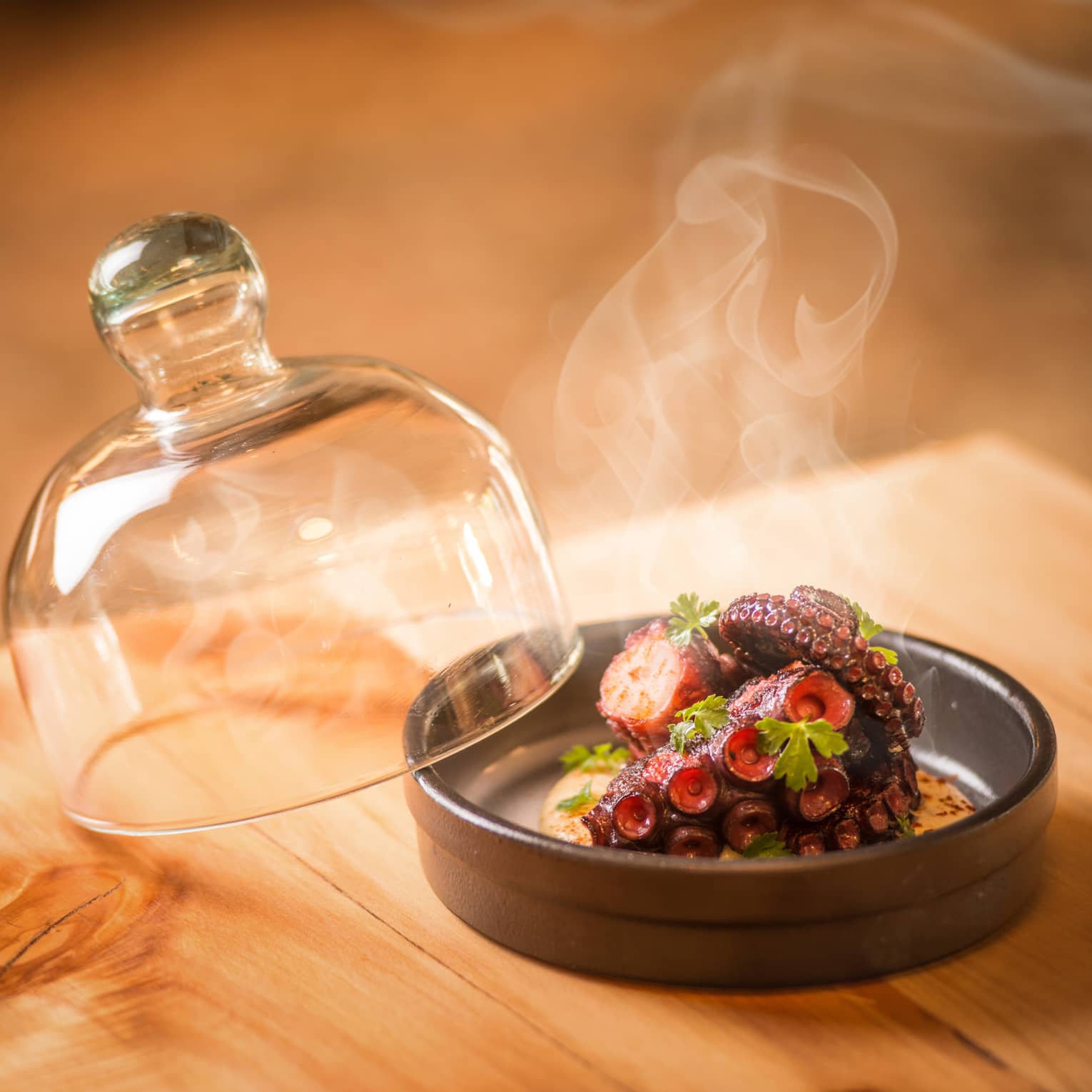Steam rises from Grilled Octopus in round black dish with glass lid