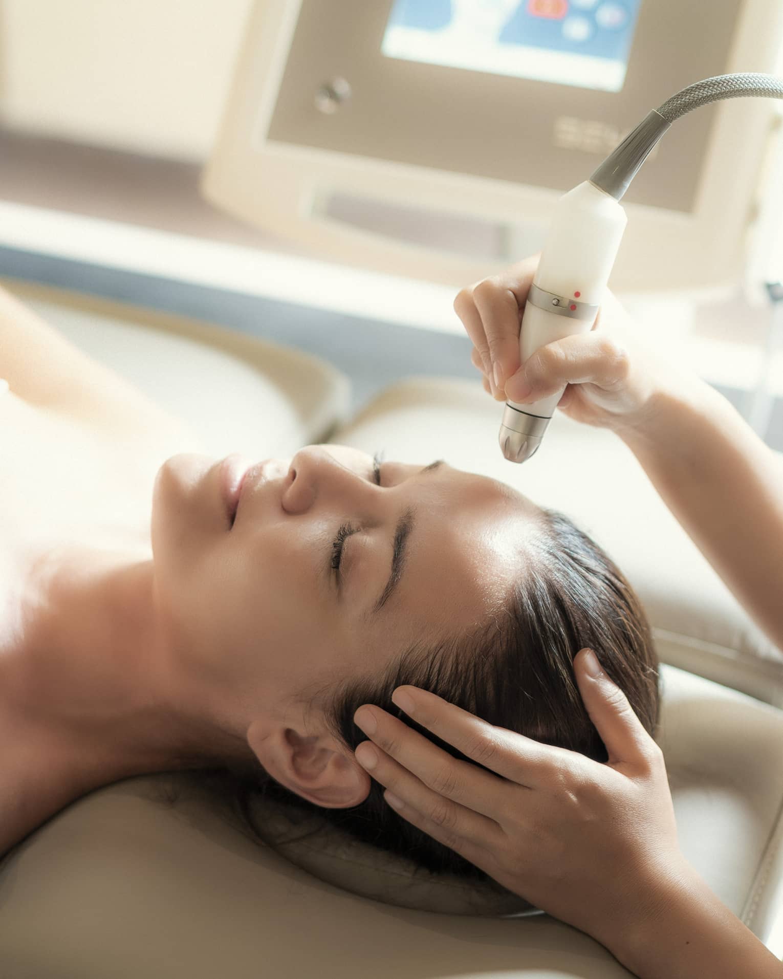 An aesthetician uses a tool on the face of a relaxing woman.