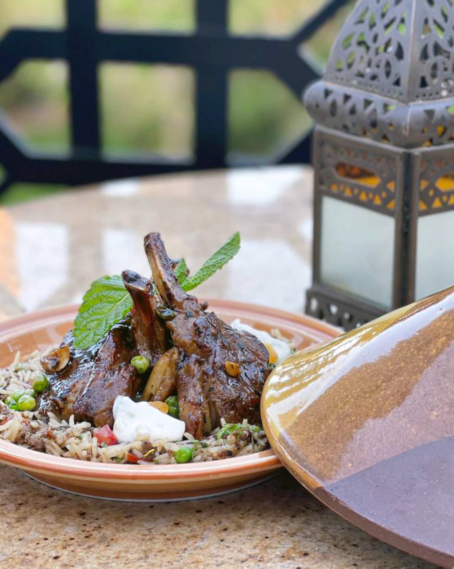 Lamb chops plated with tagine lid to the side and lantern on the table