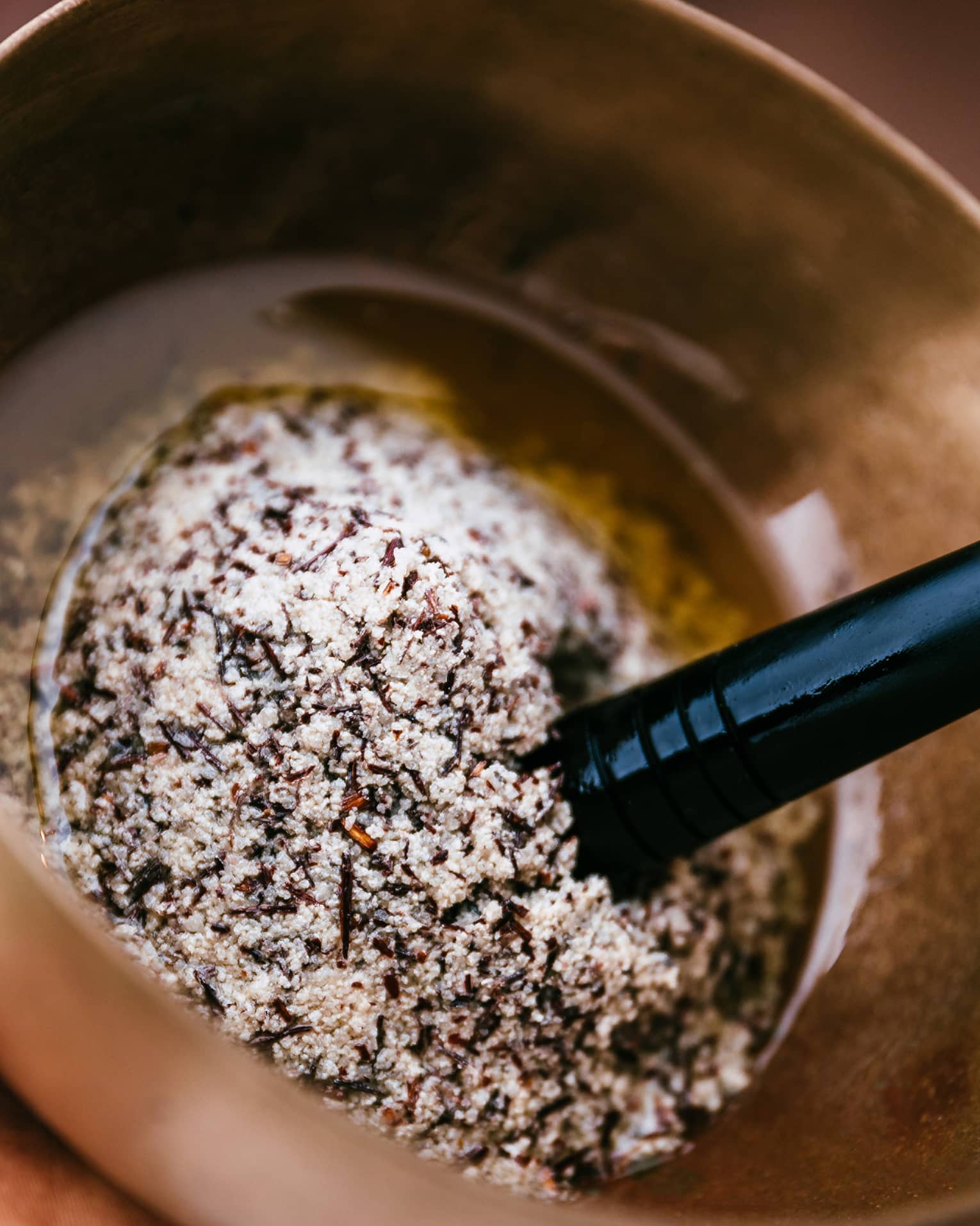 A person uses a golden mortar and pestle to grind several salts and spices into oil.