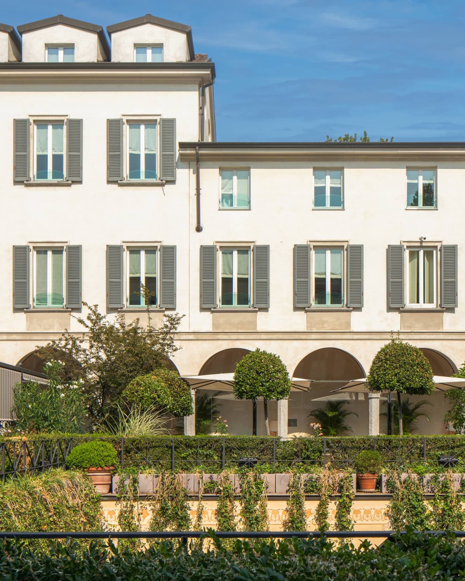 Shrubs, potted plants around rectangular courtyard garden under Four Seasons Hotel Milan building