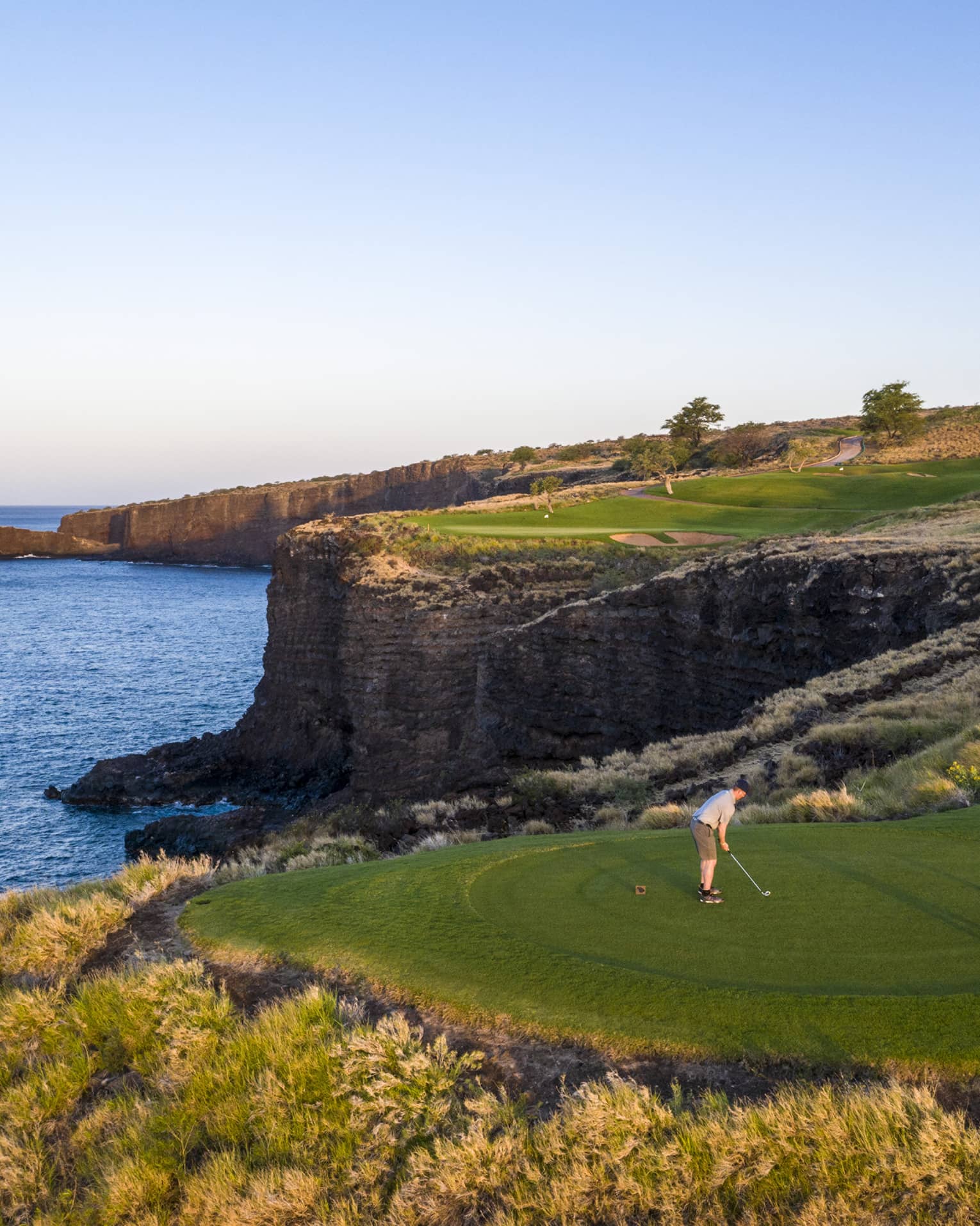 Two golfers at the 12th-hole tee at Manele Golf Course at Four Seasons Resort Lanai, cliffs and ocean in background