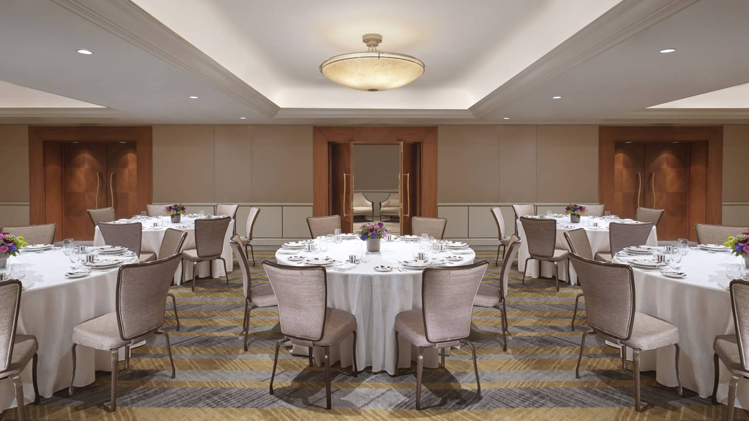 Several banquet tables with white linens, surrounded by velvet chairs.