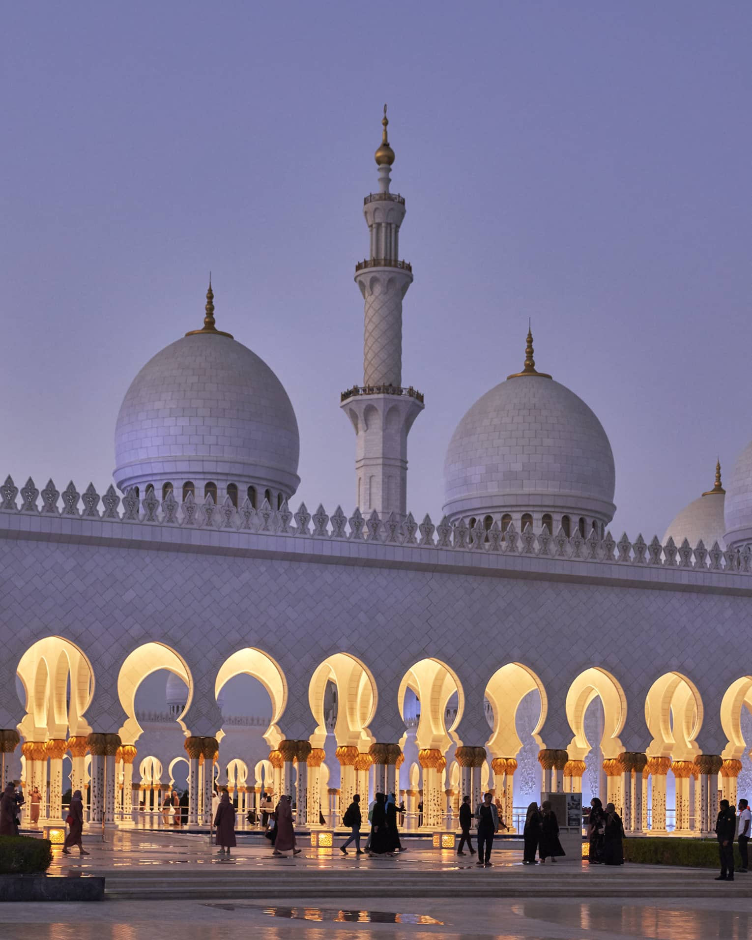 Stunning white marble mosque at dusk features a minaret with pointed domes at either side; keyhole arches line the entrance.