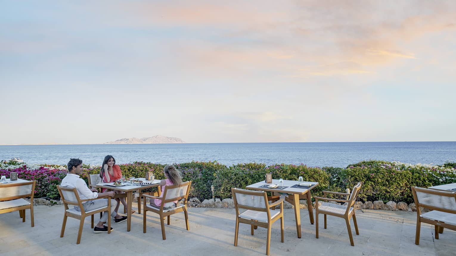 Man and woman sit at dining table on outdoor restaurant terrace, sea view