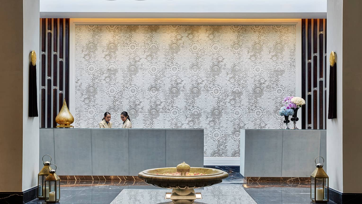 Staff at hotel reception desk in lobby with white mosaic backdrop