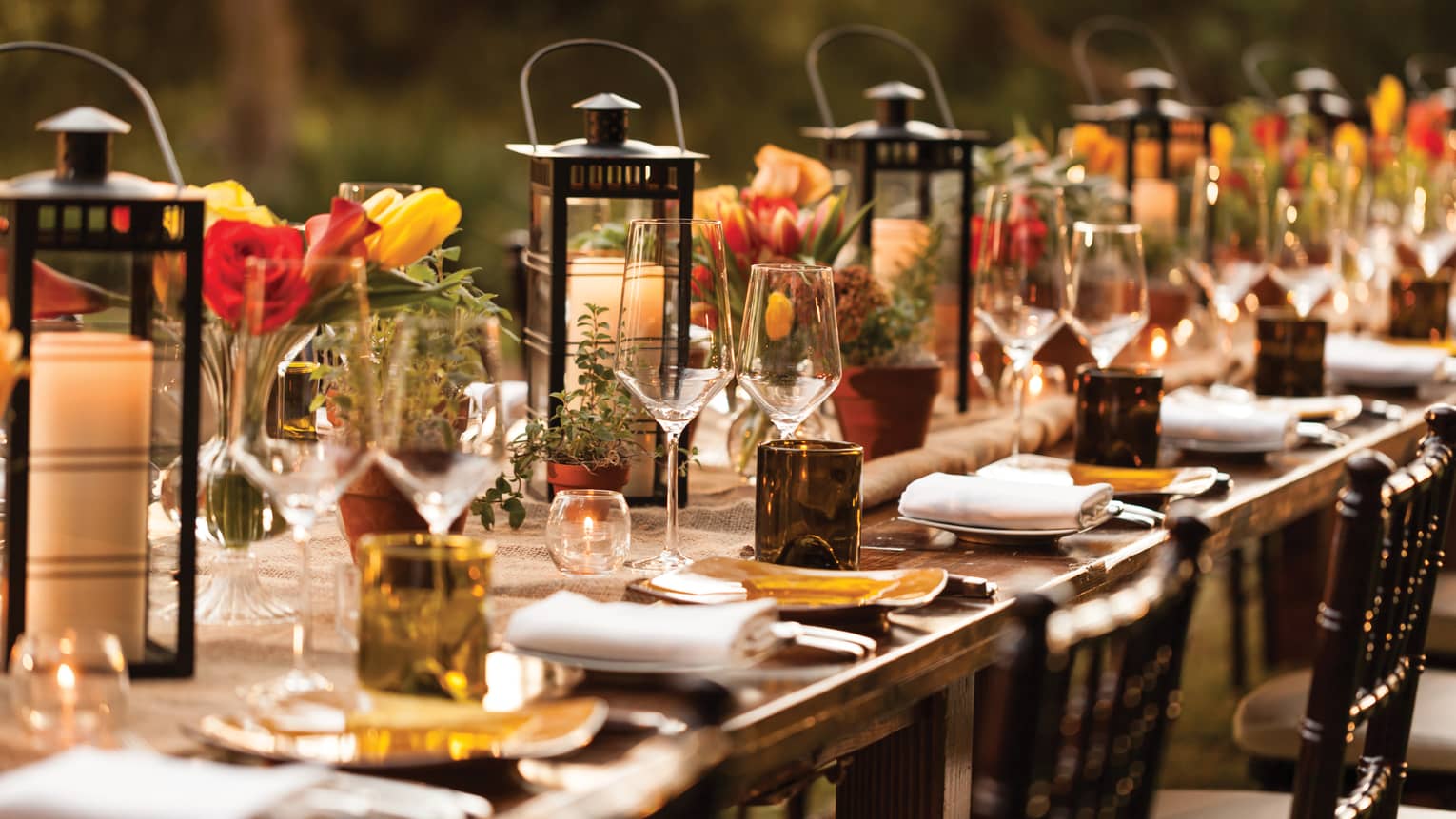 Close-up of long outdoor dining table set with lanterns, candles, wine glasses, flowers