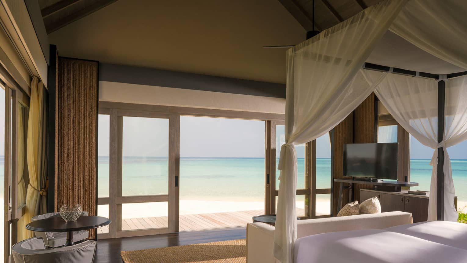 Beach Villa bedroom with white canopy bed by sliding doors to patio, lagoon views