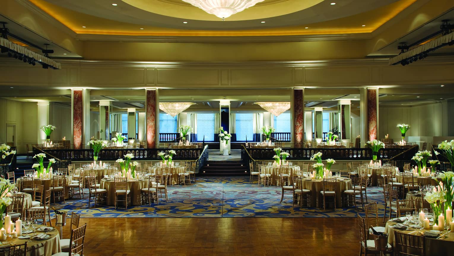 Ballroom dance floor under large cone-shaped crystal chandelier, round banquet tables