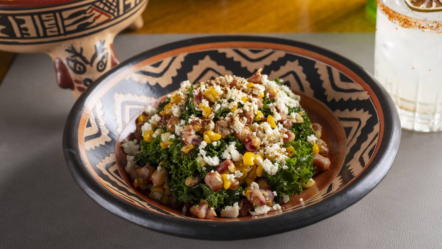 Assorted corn, kale, cuajada cheese and chipotle aioli served in a black-and-white patterned clay bowl