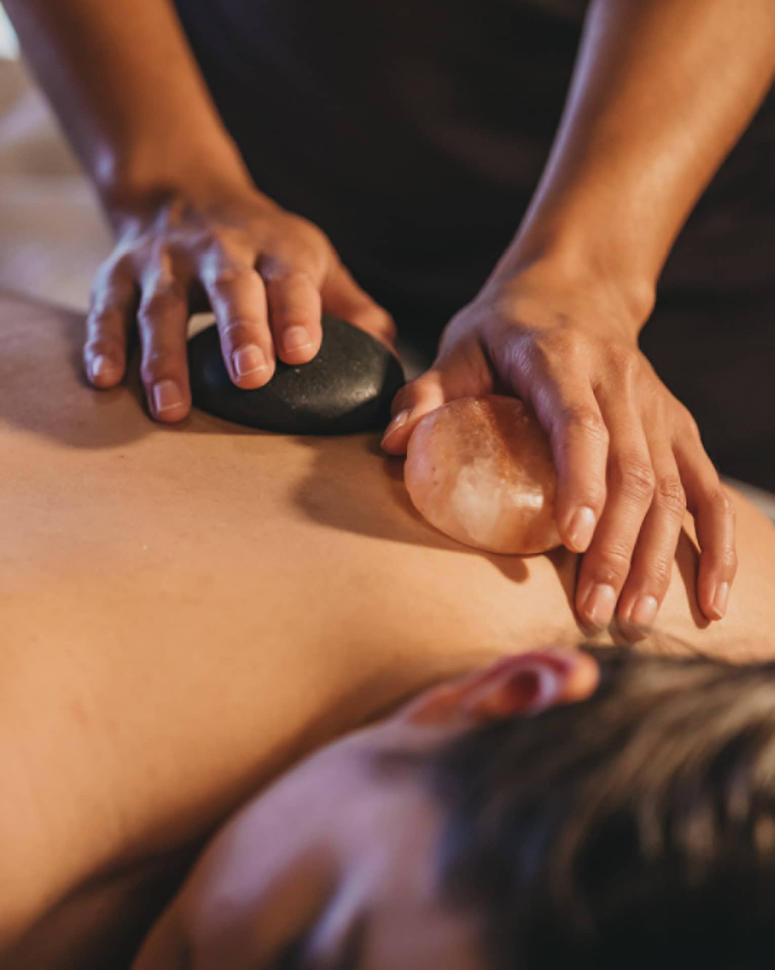 Close up of hands massaging warm stones on a woman's bare back