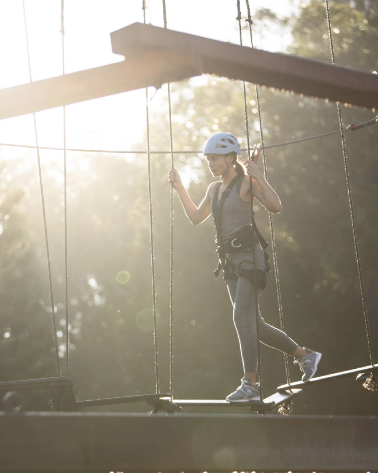 Woman walking on aerial ropes course wearing harness and helmet