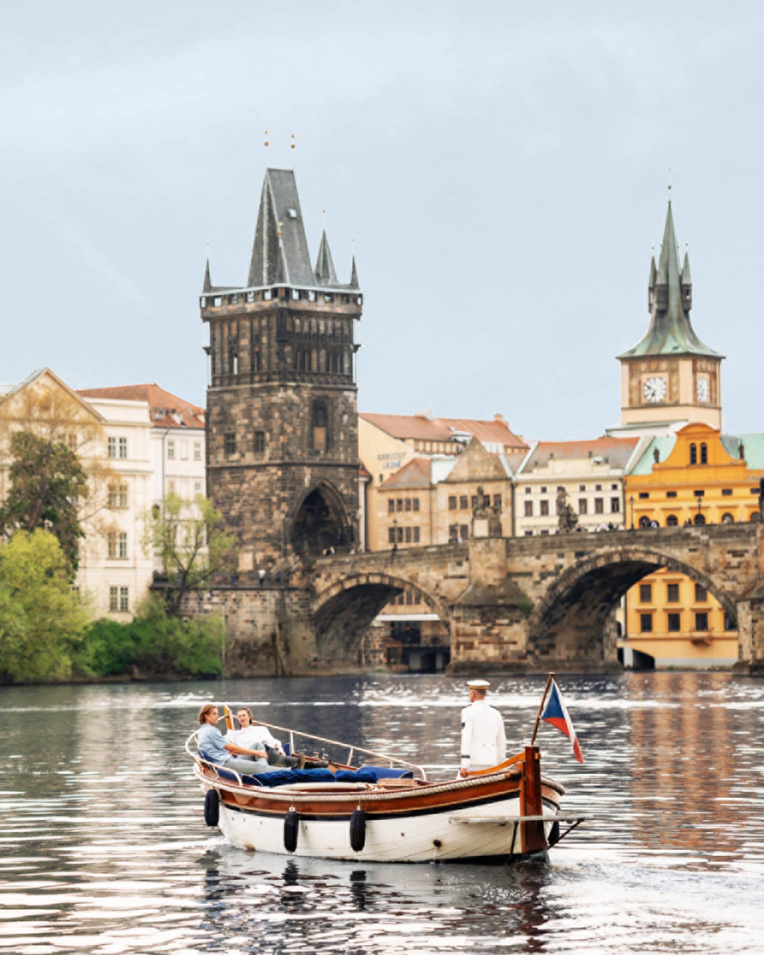 Couple in wooden boat with captain on Vltava River with baroque buildings in backdrop