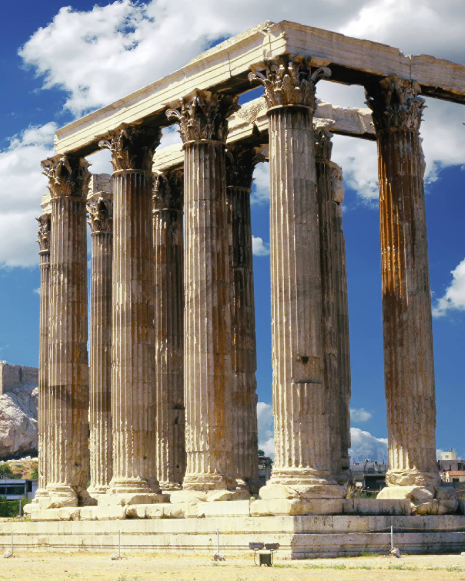 A temple with towering columns featuring intricate designs; more ruins and the Parthenon prominent in the background.